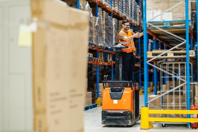 an inspector on forkflift scanning boxes on shelves in warehouse