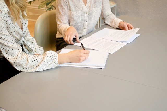 woman-signing-on-white-printer-paper-beside-woman-about-to-touch-the-documents